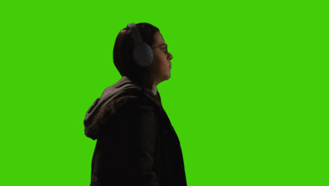 Woman-Wearing-Wireless-Headphones-Streaming-Music-From-Mobile-Phone-Walking-Across-Frame-Against-Green-Screen-1